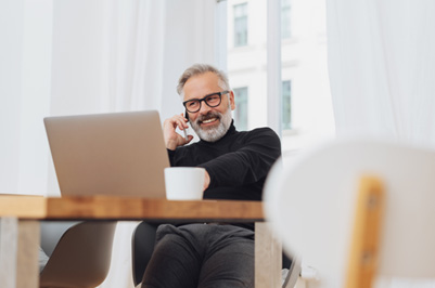 Man smiling while talking on phone and working on laptop