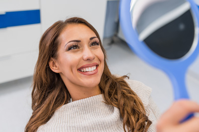 Woman smiling at reflection in handheld mirror