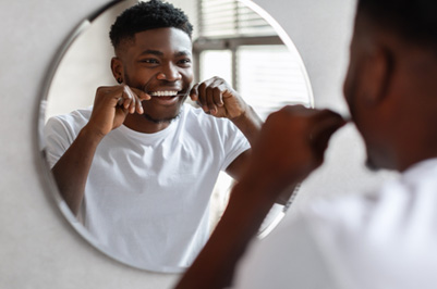 Man smiling while flossing in bathroom