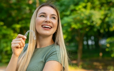 Smiling blonde woman holding a clear aligner
