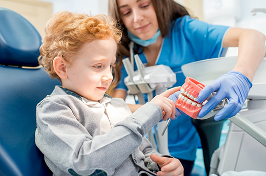 Young boy in orthodontic chair pointing to a model of the teeth
