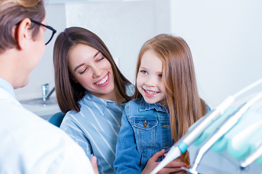 Young girl sitting on her mothers lap while visiting the dentist